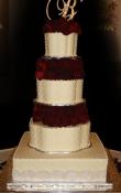 Ivory buttercream iced,  4 tier petal and square wedding cake decorated with dotted swiss and lace embossed Pearlescent scalloped ribbon . Monogram and Fresh Roses as the topper. Silver Square cake base.  (This cake can serve receptions with 160-378 expected guests)